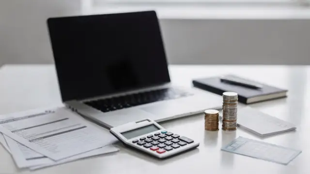Arbeitsplatz mit Laptop, Unterlagen und Münzen zum Thema Mikrokredit für die Gründung