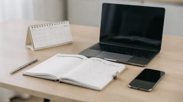 Wochenplanung eines Solo-Selbstständigen mit Kalender, Laptop und Notizbuch auf dem Schreibtisch